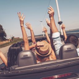 Just fun and road ahead. Rear view of young happy people enjoying road trip in their convertible and raising their arms up